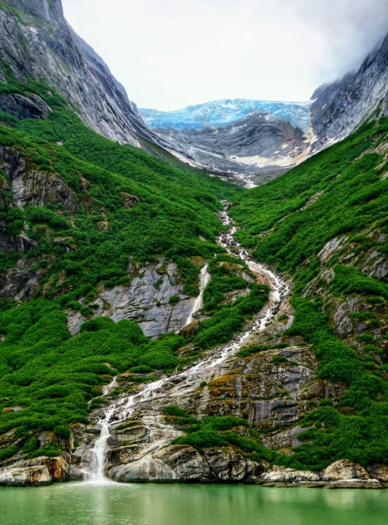 Vattenfall i Alaska längs gröna berg